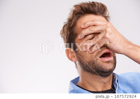 Oh no. Studio shot of a handsome young man covering his eyes in regret against a gray background. Oh no. Studio shot of a handsome young man covering his eyes in regret against a gray background. 107572924