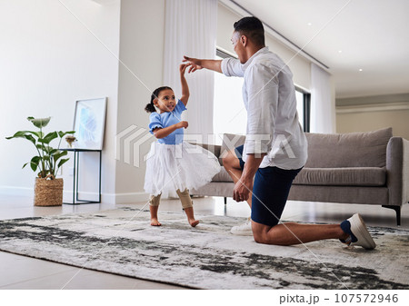 Family, father and daughter dancing for fun, energy and love in the living room feeling happy holding hands to dance at home. Man or dad and girl child moving to favorite song on fathers day in house 107572946
