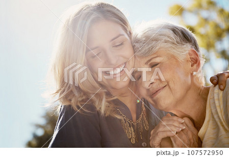 Family, love or smile with a senior mother and daughter bonding outdoor together during a summer day. Happy, flare and retirement with a young man hugging her elderly parent outside in the park 107572950