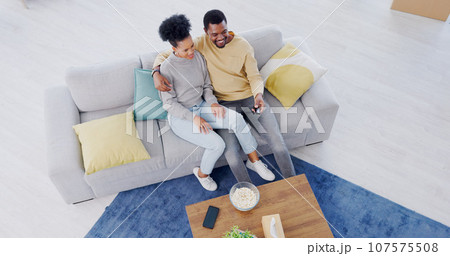 Black couple, top view and couch in living room, tv and relax with popcorn, movies and funny comedy. Man, woman and hug for bonding together, streaming and happy in lounge, couch and remote control Black couple, top view and couch in living room, tv and relax with popcorn, movies and funny comedy. Man, woman and hug for bonding together, streaming and happy in lounge, couch and remote control 107575508