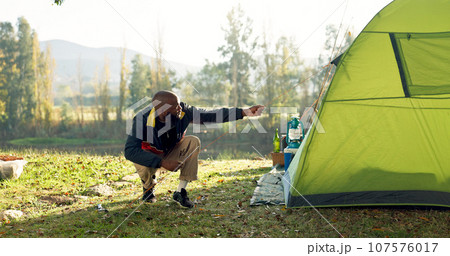 Camping, tent and black man setup in nature for shelter on outdoor holiday, vacation and adventure, Campsite, traveling and male person with hammer for pins for gear in woods, forest and countryside 107576017