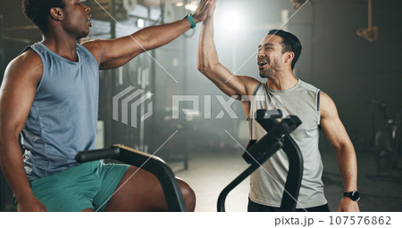 Man, cycling and personal trainer in high five, motivation or fitness workout, exercise and training at gym. Trainer coaching male person on bicycle, machine or equipment in cardio at health club 107576862