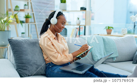 Video call, laptop and black woman doing remote work on couch in a home writing notes in webinar or e learning. Sofa, information and student working with online technology in apartment for research 107576919