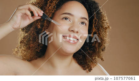 Happy woman, pipette and face serum for skincare, cosmetics or glow against a studio background. Female person smile applying facial oil in dermatology, beauty or skin treatment in health or wellness 107577061