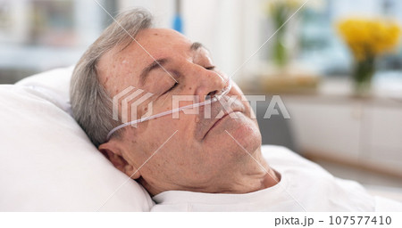 Oxygen, hospital bed and senior man sleeping with ventilation and breathing tube support in a clinic. Elderly patient, medical care and emergency room with male person at a doctor for healthcare Oxygen, hospital bed and senior man sleeping with ventilation and breathing tube support in a clinic. Elderly patient, medical care and emergency room with male person at a doctor for healthcare 107577410