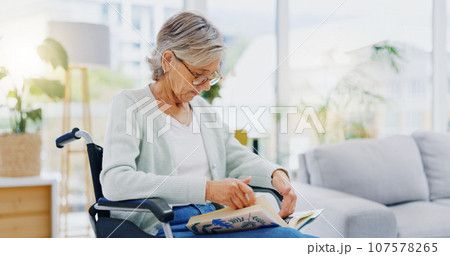 Senior woman, book and reading to relax in living room for story, novel and knowledge. Elderly female in wheelchair, enjoying books and focus in lounge for retirement break, literature and hobby at r 107578265