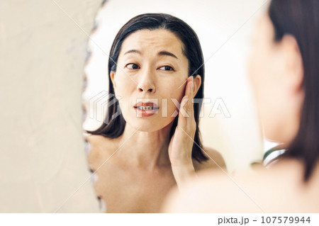 肌が気になって鏡を見るミドル女性 107579944
