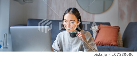 Portrait of asian businesswoman smiling, working on laptop from home, remote online studying in her living room 107580086