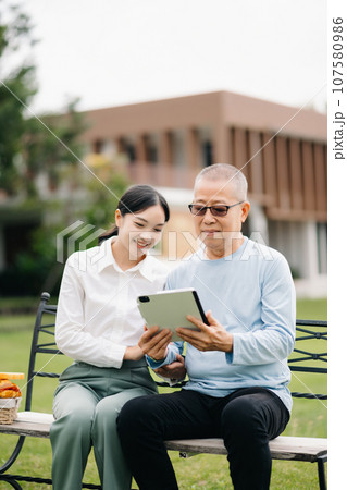Happy adult granddaughter and senior grandfather having fun enjoying talk while relaxing sitting outdoor in the park. 107580986