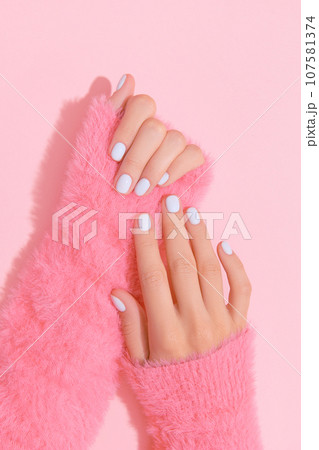 Womans hands with white nail design on pink background 107581374