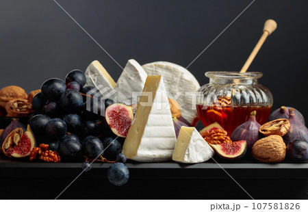 Camembert cheese with fruits and honey on a black background. 107581826