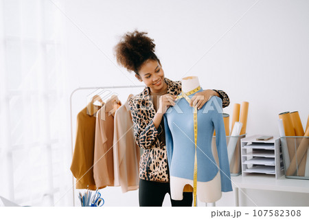 Calm curly brunette dark skinned woman on desk in office of fashion designer and holds tablet and smartphone.. 107582308