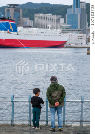 老人と孫と思われる子供。子供に釣りを教えている。背景は神戸市街地。神戸ポートアイランドで撮影 老人と孫と思われる子供。子供に釣りを教えている。背景は神戸市街地。神戸ポートアイランドで撮影 107583738