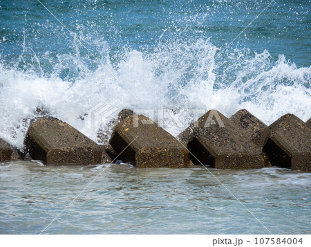 海岸の消波ブロックに波が打ち寄せて波飛沫が上がる。 107584004