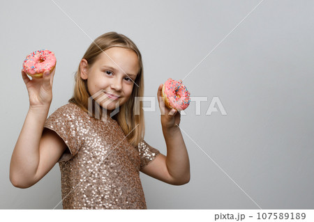 Cute smiling child girl with tasty pink donut on gray background. Holiday birthday party concept Cute smiling child girl with tasty pink donut on gray background. Holiday birthday party concept 107589189