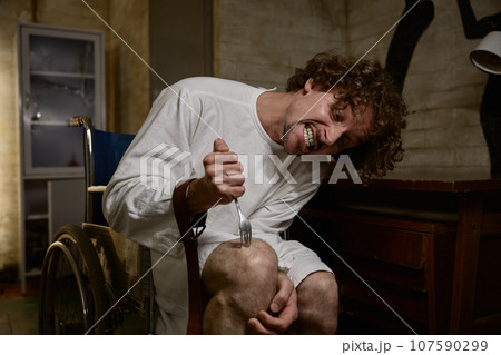 Mad raving lunatic hurting himself, stabbing his knee with metal fork Mad raving lunatic hurting himself, stabbing his knee with metal fork 107590299