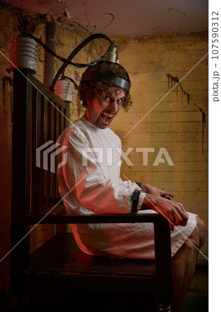 Crazy man screaming feeling madness on electric chair at psychiatric hospital Crazy man screaming feeling madness on electric chair at psychiatric hospital 107590312