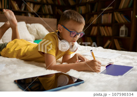 Little boy child using modern gadget studying at home lying in bed 107590334