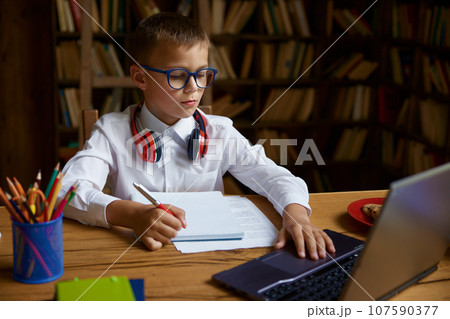 Little boy child studying at home table sitting front of computer laptop Little boy child studying at home table sitting front of computer laptop 107590377