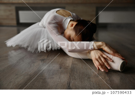 Young graceful ballerina dressed tutu posing on floor while training in studio 107590433