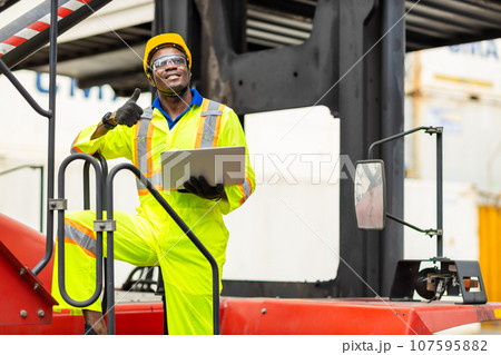African male dock worker control loading containers cargo at warehouse container shipyard. Marine and carrier staff employee. cargo loading operator shipping export logistics ship yard. African male dock worker control loading containers cargo at warehouse container shipyard. Marine and carrier staff employee. cargo loading operator shipping export logistics ship yard. 107595882