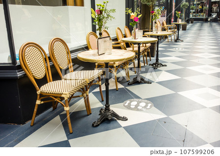 カフェの店先に置かれた木枠の椅子とテーブルと飾られた花 ウエールズの街カーディフのアーケードにて カフェの店先に置かれた木枠の椅子とテーブルと飾られた花 ウエールズの街カーディフのアーケードにて 107599206