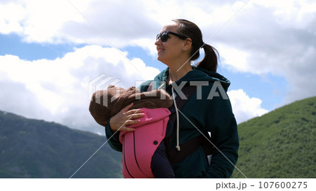 Cheerful young mother hiker with baby carrier hiking in mountains. Active travel with family and adventure concept 107600275