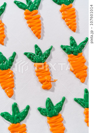 Piping melted chocolate from a piping bag over the parchment paper to make chocolate carrot cake toppers. 107601014
