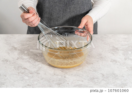 Mixing wet ingredients in a small glass mixing bowl to bake banana cookies with chocolate drizzle. 107601060