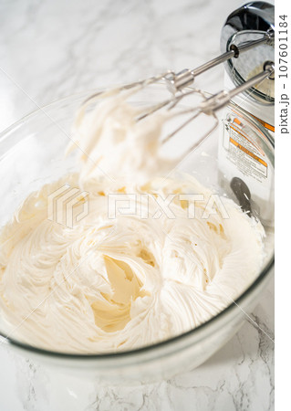 Whisking buttercream frosting in a glass mixing bowl with an electric hand mixer to prepare the peppermint buttercream frosting. 107601184