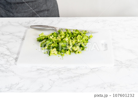 Chopping freshly steamed broccoli on a white cutting board. 107601232