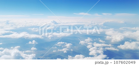 Panoramic view of fields and clouds from an airplane window. The sky is a bright blue with fluffy white clouds. 107602049