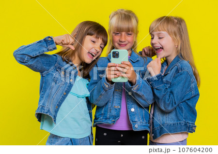 Three girls siblings friends use smartphone celebrate, playing online game, great big win good news 107604200