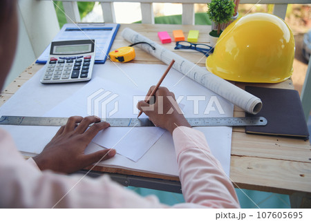 Civil construction engineer working with laptop at desk office with white yellow safety hard hat at office on construction site. Asian young man architecture project manager sitting at office on site Civil construction engineer working with laptop at desk office with white yellow safety hard hat at office on construction site. Asian young man architecture project manager sitting at office on site 107605695