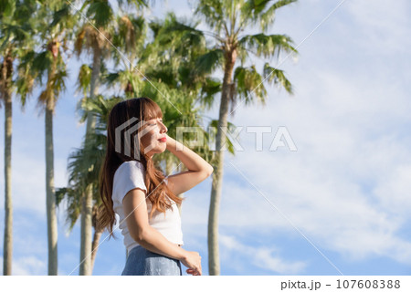 ヤシの木をバックに夕日を浴びる女性 107608388