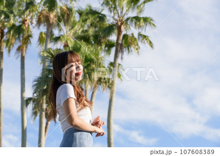 ヤシの木をバックに夕日を浴びる女性 107608389