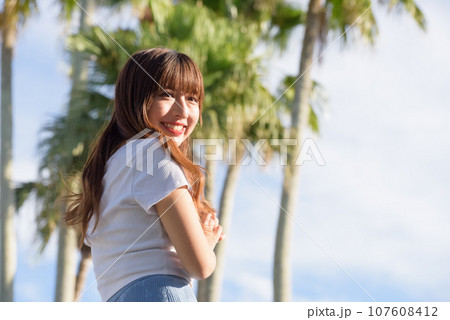 ヤシの木をバックに夕日を浴びる女性 ヤシの木をバックに夕日を浴びる女性 107608412