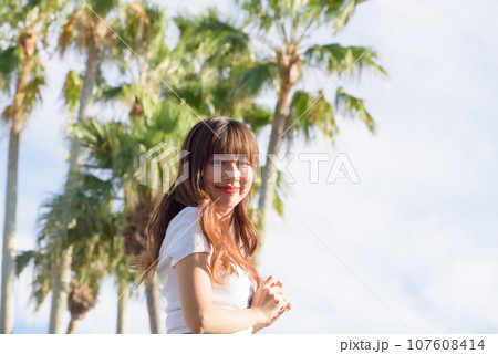 ヤシの木をバックに夕日を浴びる女性 107608414