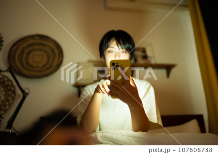 女性は夜中にスマートフォンを見ている。 女性は夜中にスマートフォンを見ている。 107608738