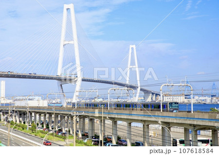 名古屋市、名港トリトンをバックに金城ふ頭駅付近を走るあおなみ線電車 107618584