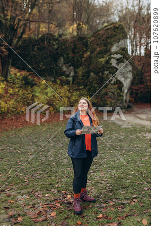 Positive cheerful girl holding paper map over nature background. Mountain peaks. Freedom, happiness, travel and vacations concept, outdoor activities, full body Positive cheerful girl holding paper map over nature background. Mountain peaks. Freedom, happiness, travel and vacations concept, outdoor activities, full body 107620899