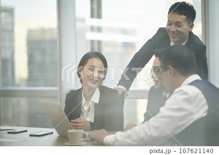 through-the-glass shot of a team of four asian corporate executives meeting in office discussing business 107621140