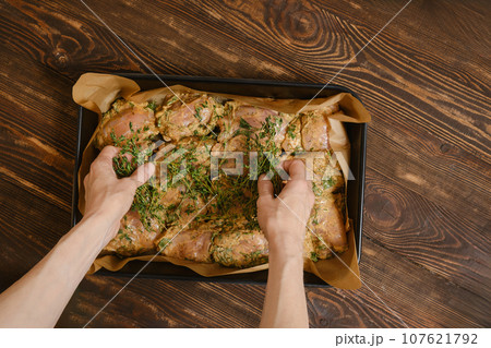 Hands of woman scattering thyme over chicken thighs in baking tray 107621792