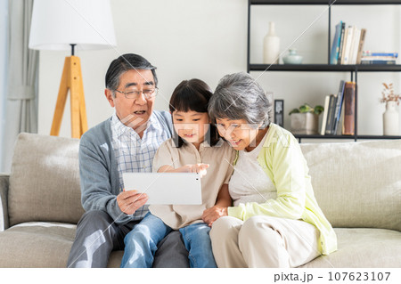 リビングでタブレットを見る孫娘とシニアの夫婦 リビングでタブレットを見る孫娘とシニアの夫婦 107623107