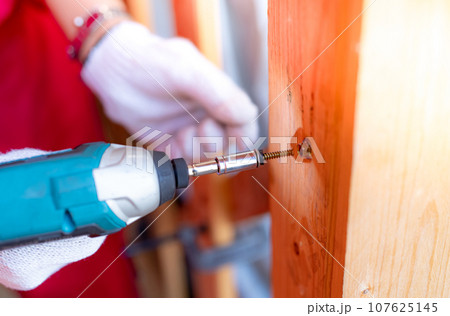 Carpenter and screwdriver hand tool. A skilled worker set to work drilling and installing wooden fixtures, using electric screwdriver to construct and repair parts of house with precision and care. 107625145