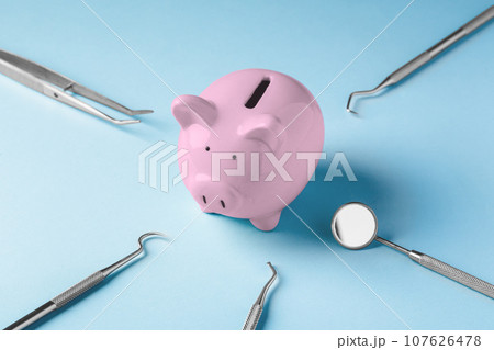 Pink piggy bank with dental instruments on blue background, dental health care and treatment cost 107626478