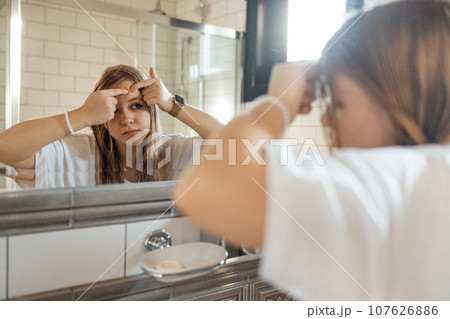 Cute teenage girl squeezes out a pimple on her cheek in the bathroom Cute teenage girl squeezes out a pimple on her cheek in the bathroom 107626886