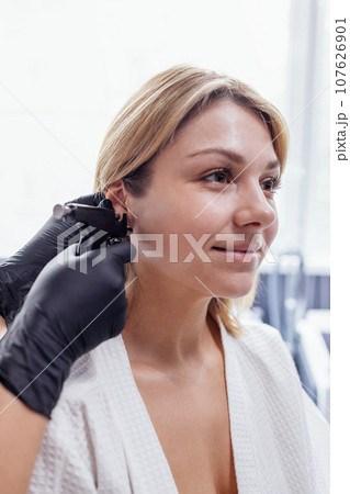 Close up of face of young blonde woman doing ear piercing procedure 107626901