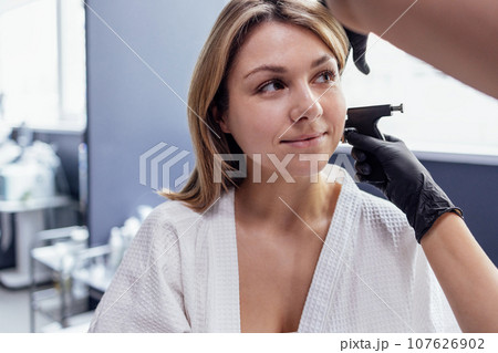 Close up of face of young blonde woman doing ear piercing procedure 107626902