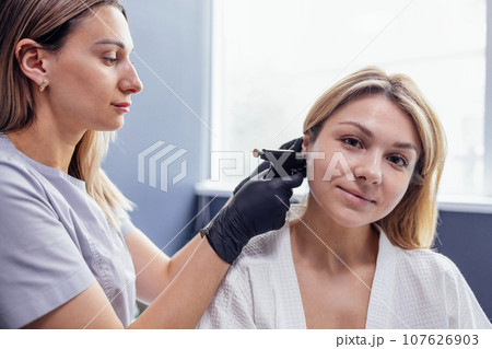 Close up of face of young blonde woman doing ear piercing procedure 107626903